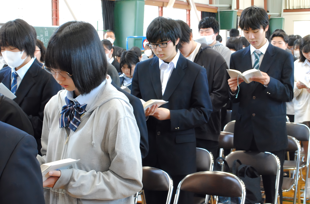 体育館で立って聖書を読む学生たちの写真（小1）